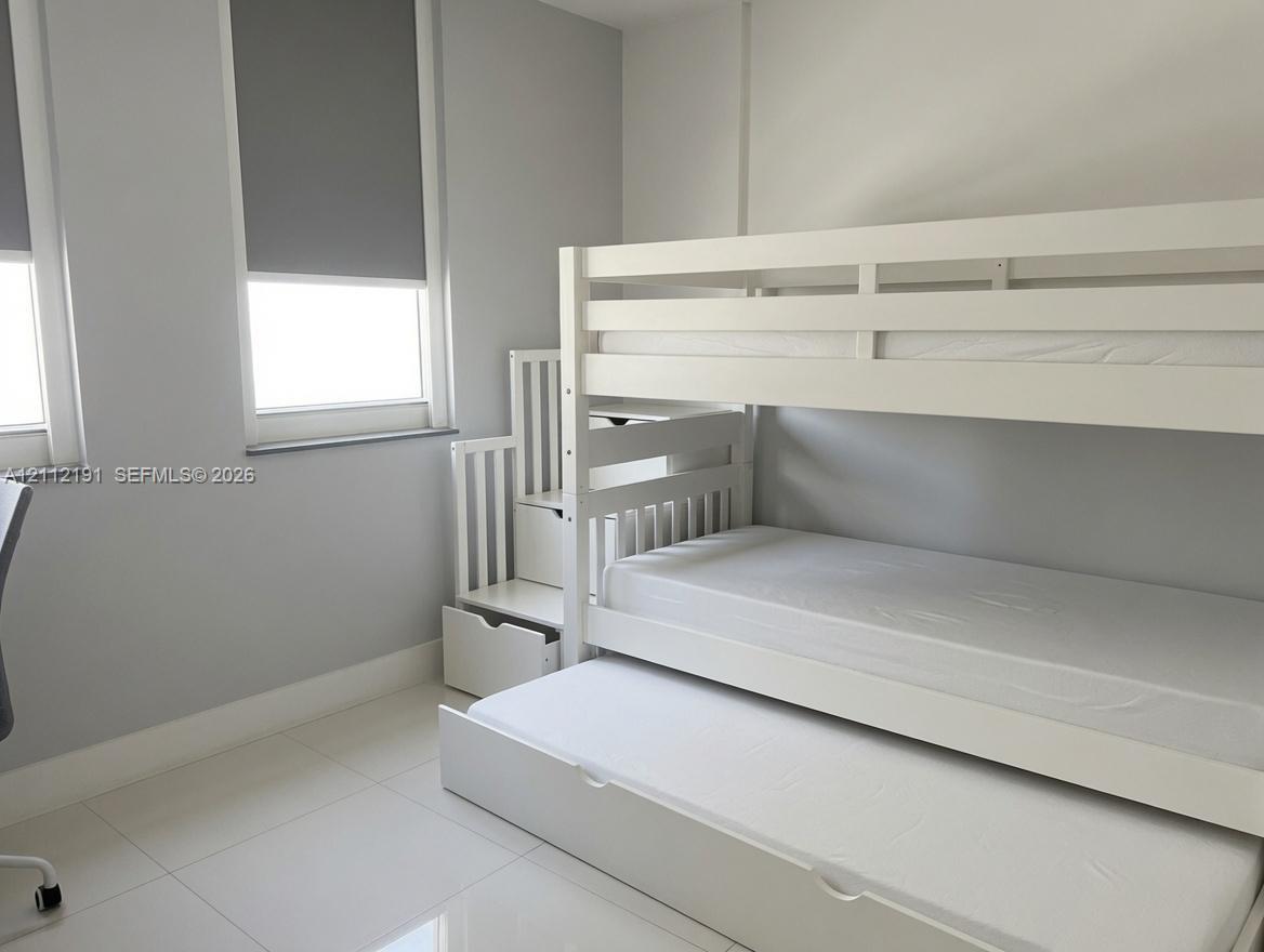 Neutral-toned room featuring large windows with roller shades, smooth-finish ceramic tile flooring, and light-reflecting wall paint