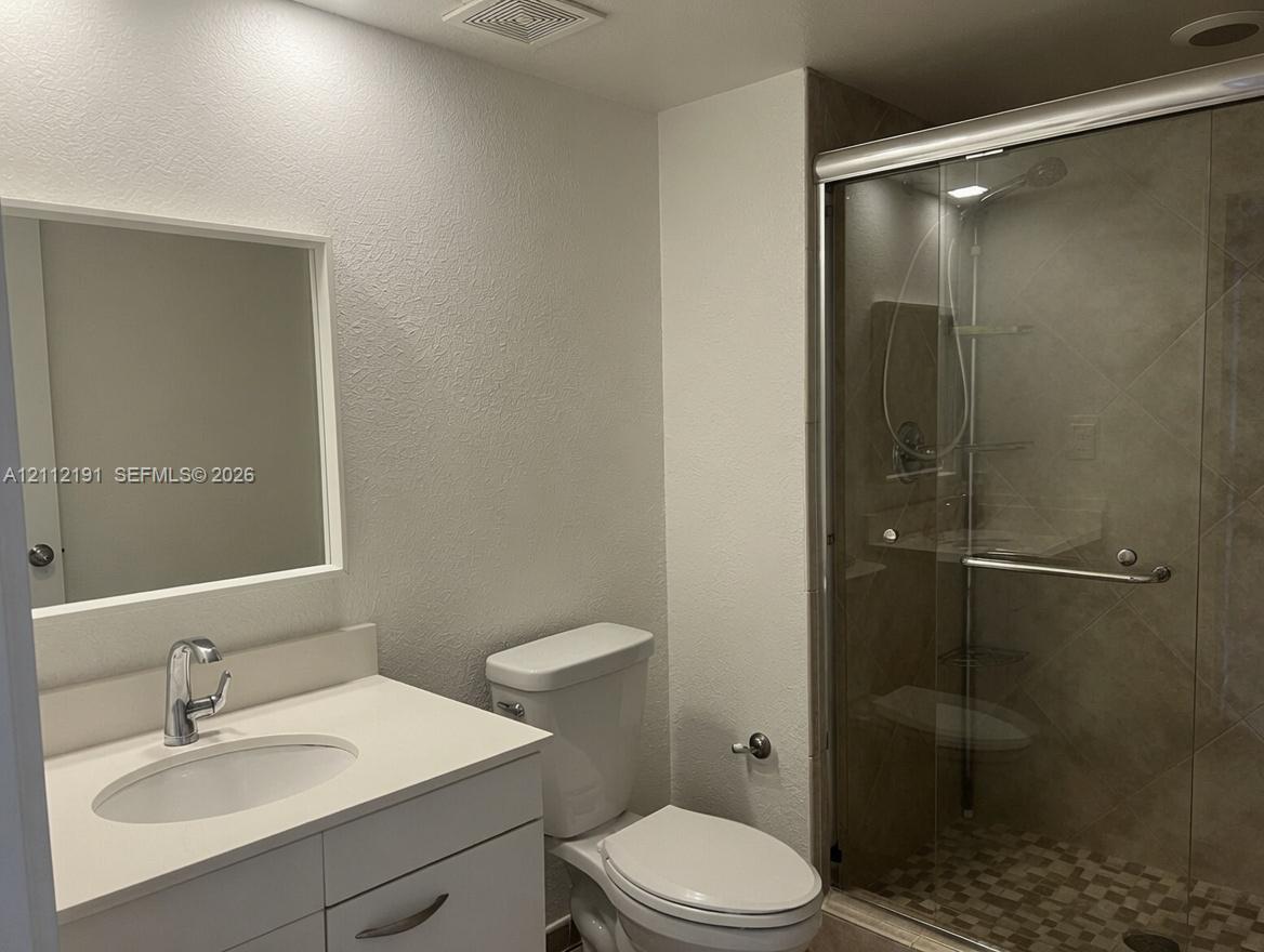 Bathroom featuring a white vanity cabinet, solid-surface countertop with an integrated basin, framed wall mirror, and a walk-in shower with a sliding glass door and tile surround