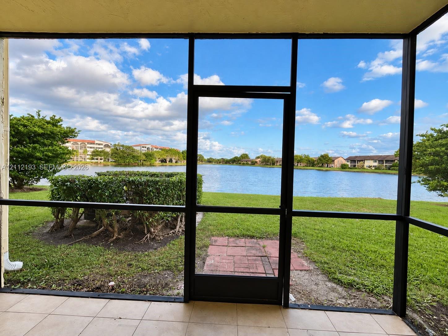 Screened-in patio with tile flooring, featuring metal framing, a direct exit to a grass yard, and a brick paver landing