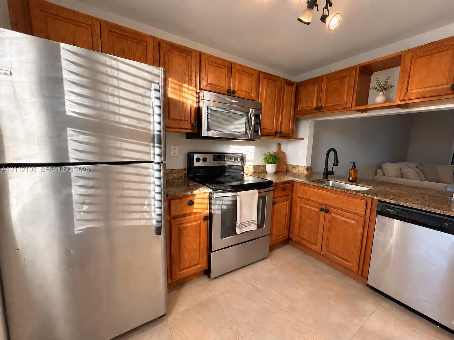 Kitchen featuring wood cabinetry, stone countertops, stainless steel appliances, a deep-basin sink with a matte black faucet, and tile flooring