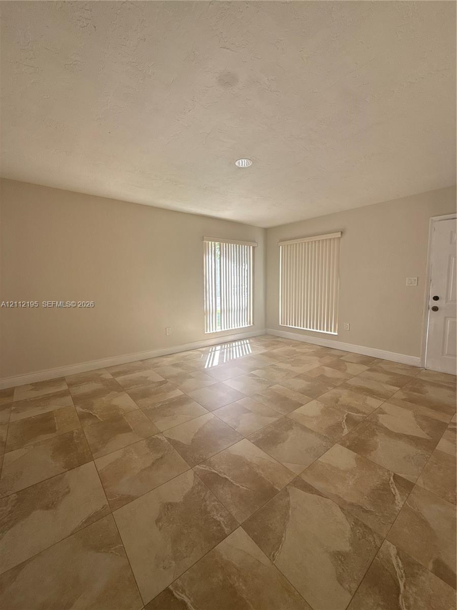 Neutral-toned interior space featuring large-format ceramic tile flooring, two windows with vertical blinds, and a recessed ceiling light fixture