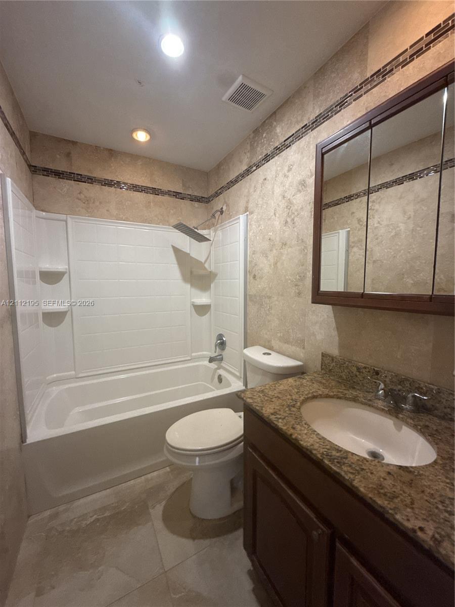 Bathroom featuring stone-finish wall tiling with mosaic accent borders, a built-in vanity with an integrated basin, a stone-finish countertop, and a rainfall showerhead