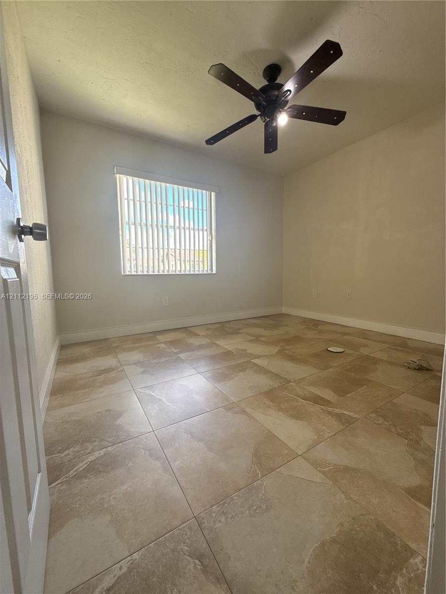 Neutral-toned large-format tile flooring, multi-blade ceiling fan with integrated lighting, and vertical window blinds