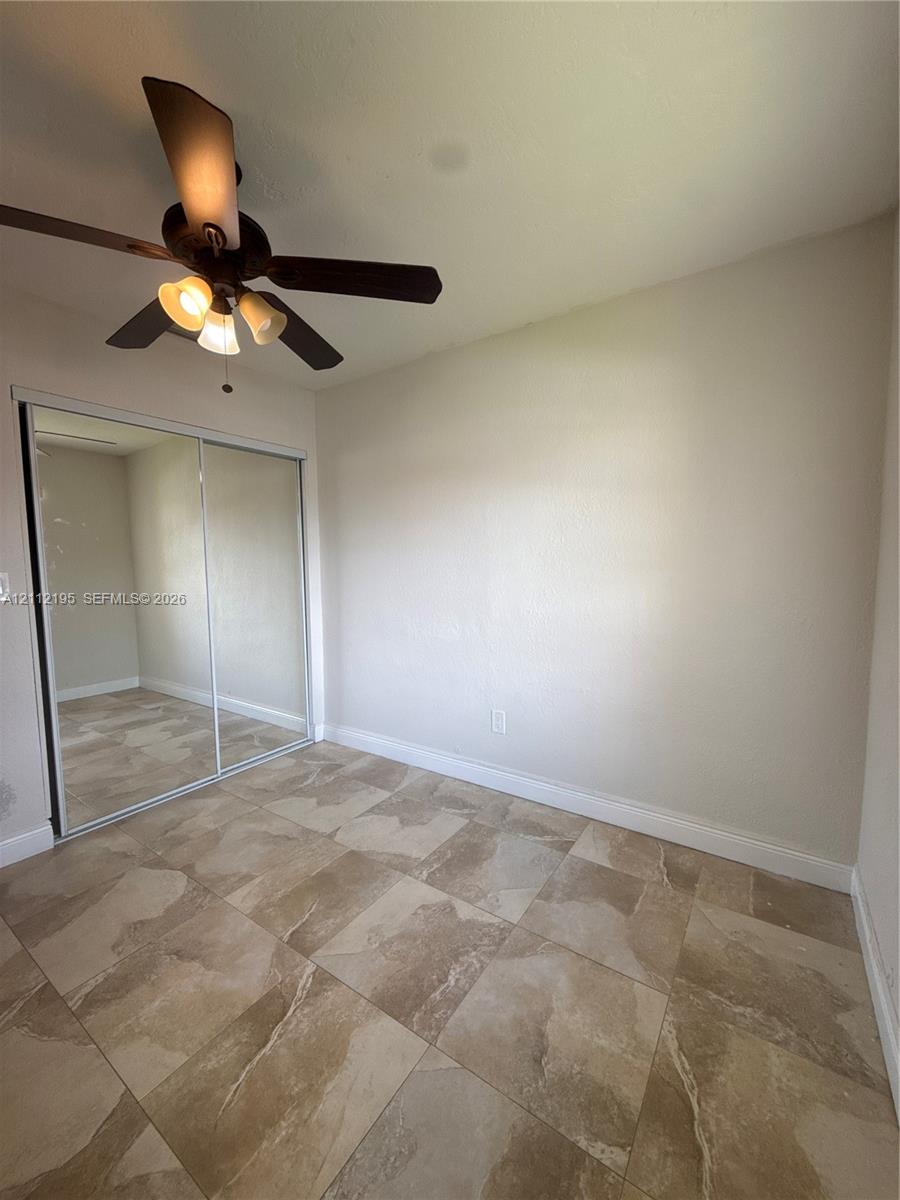 Room featuring large-format tile flooring, mirrored sliding closet doors, and a ceiling-mounted light fixture with a multi-blade fan