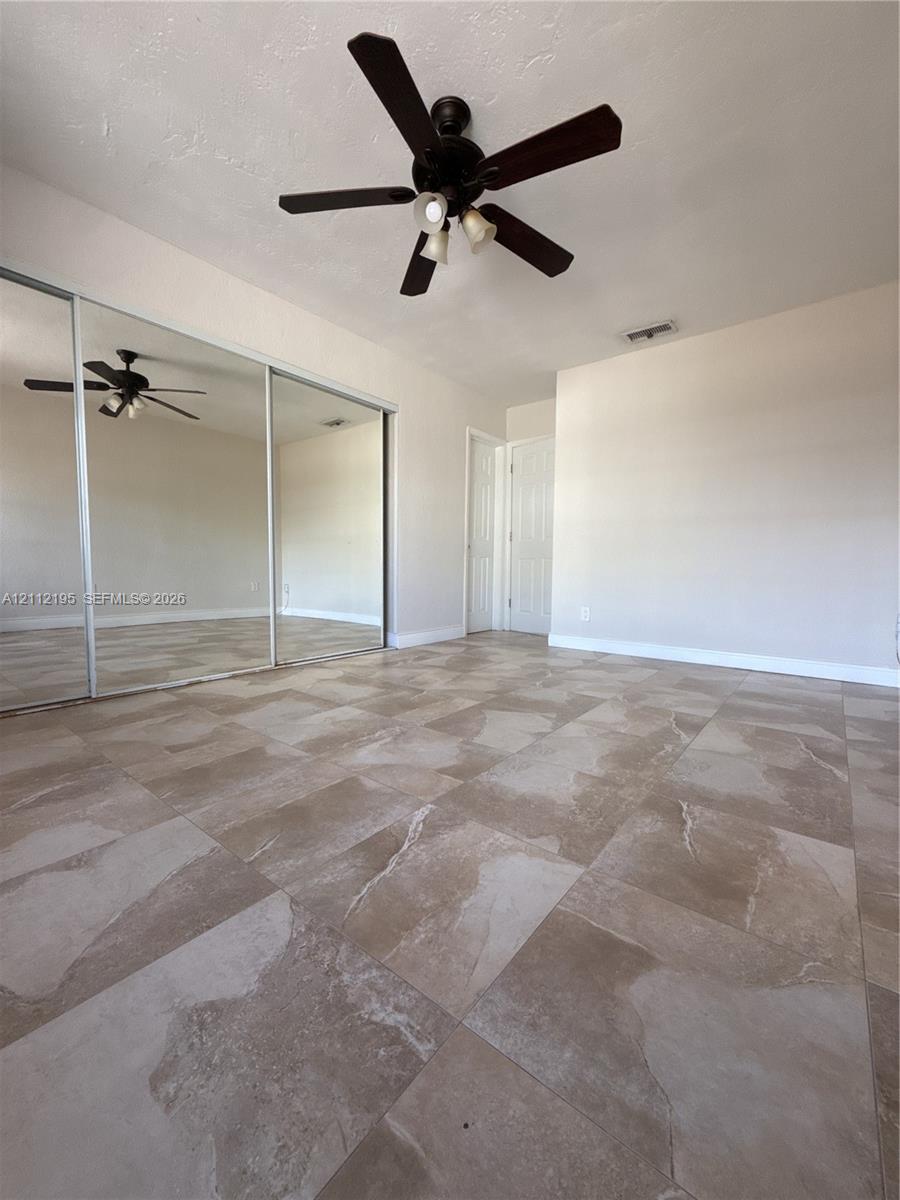 Large-format tile flooring, ceiling fan with integrated lighting, and wall-to-wall sliding mirrored closet doors