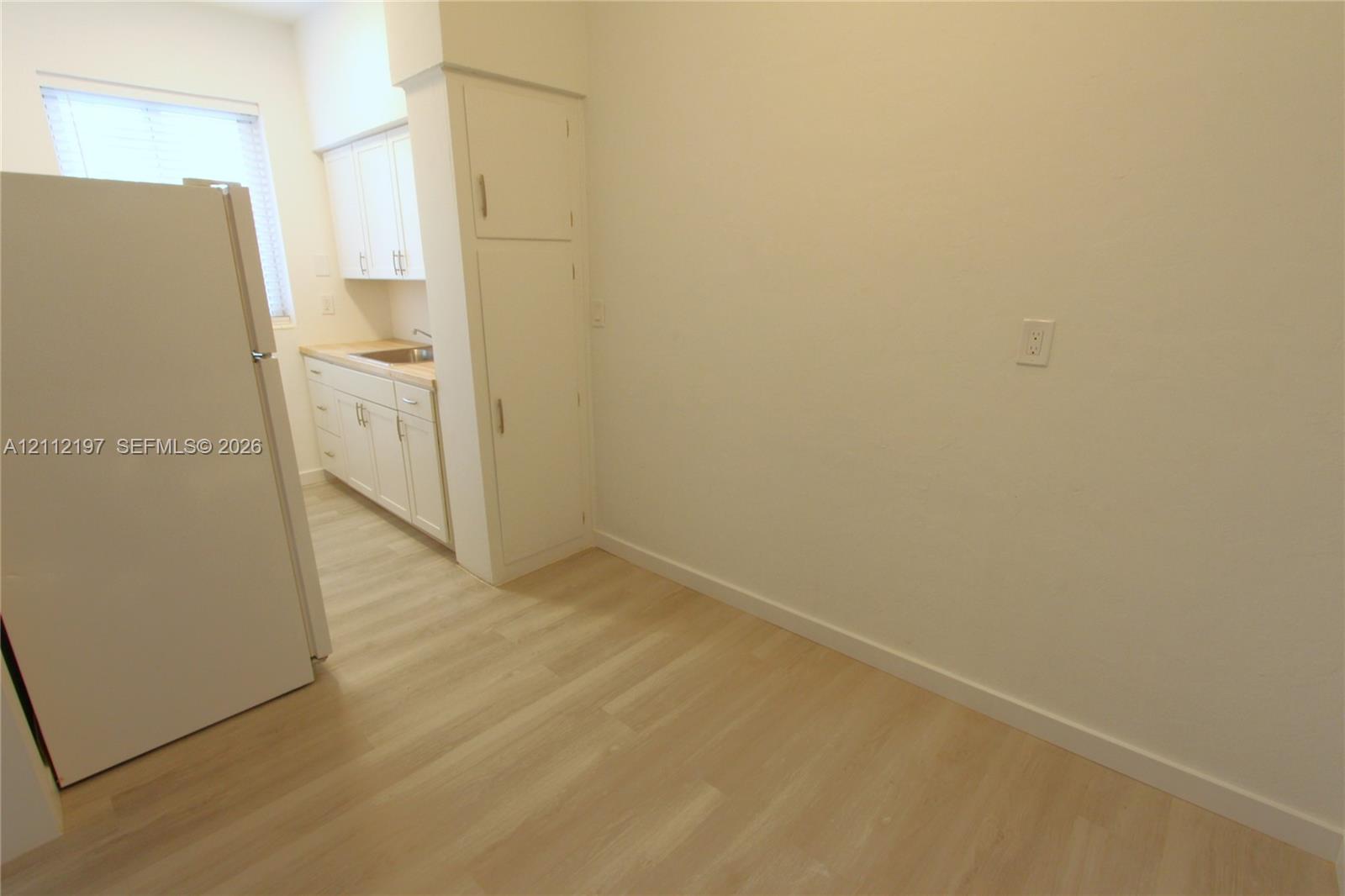 Kitchen featuring wood-finish flooring, white cabinetry with integrated storage, and a stainless steel sink