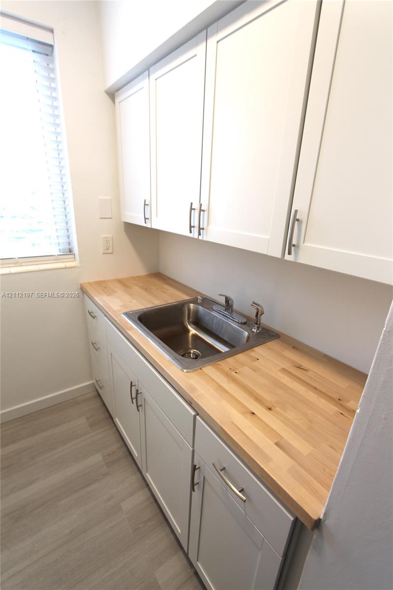 White shaker-style cabinetry with metallic pulls, butcher-block countertop, stainless steel undermount sink, and wood-finish flooring