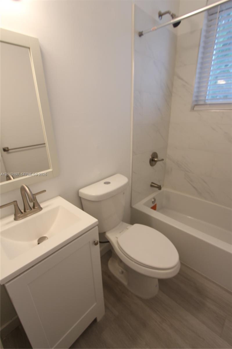 Bathroom featuring a single-sink vanity with a rectangular basin, wood-finish flooring, and a tub-shower combination with light-toned wall tile