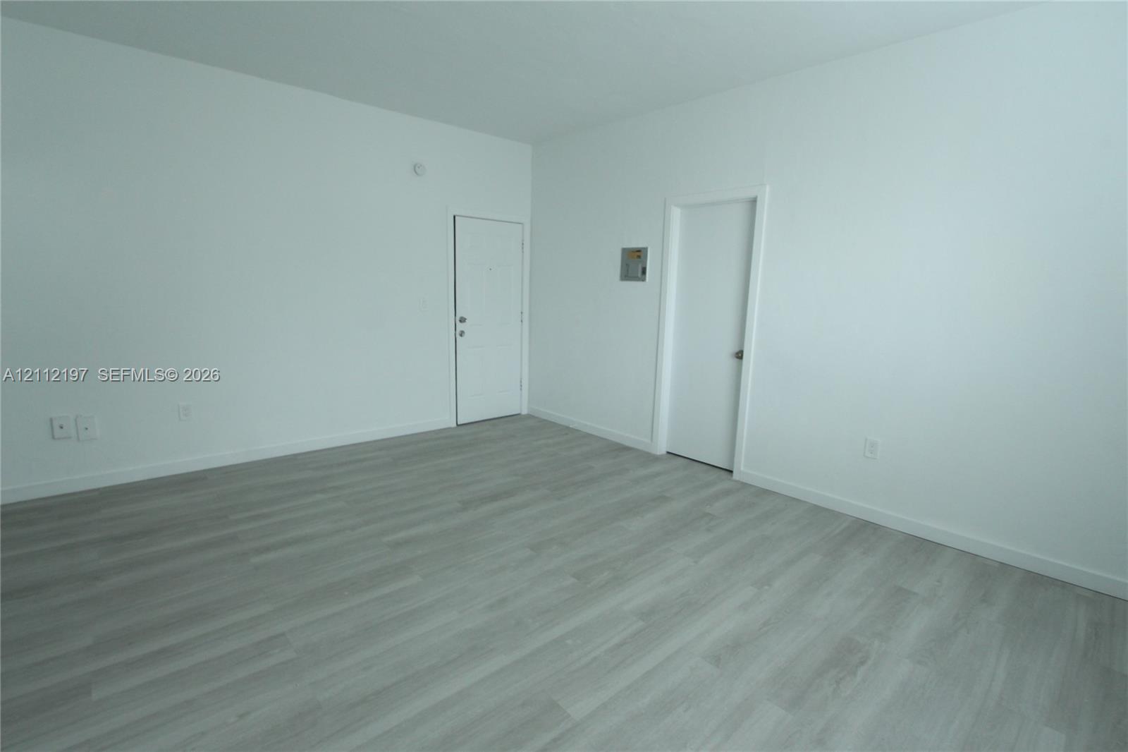 Neutral interior room featuring wood-finish flooring, smooth white wall finishes, and two solid-core doors