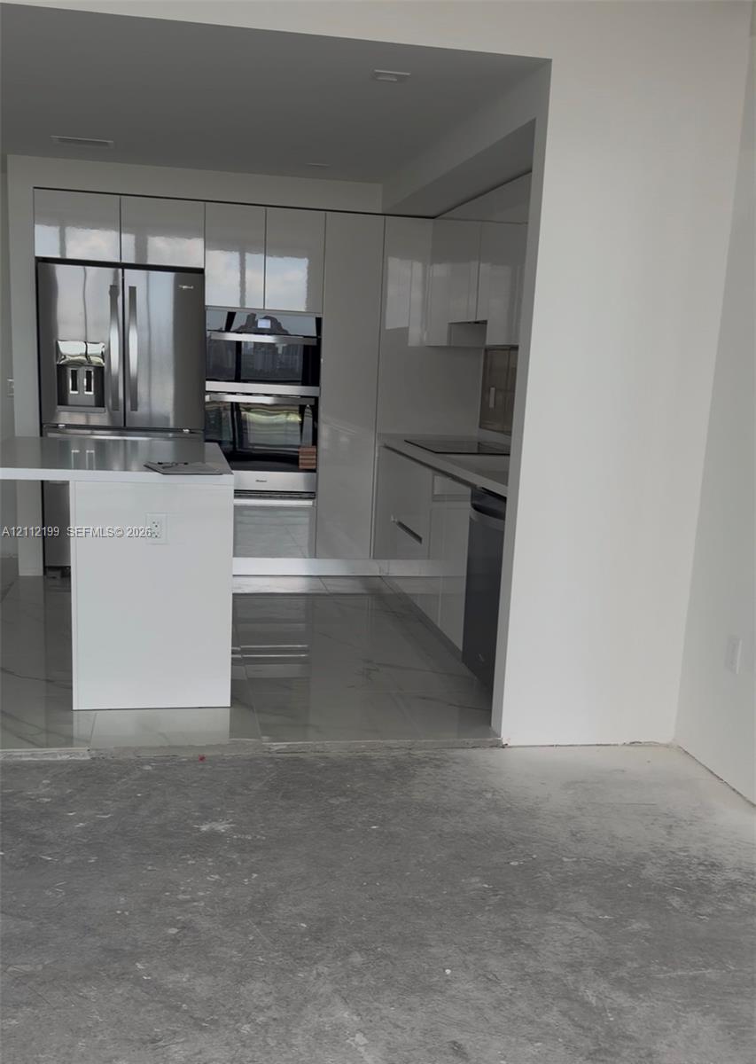 Kitchen featuring high-gloss cabinetry, stone-surface countertops, an integrated island, built-in stainless steel appliances, and tile flooring Kitchen featuring high-gloss cabinetry, stone-surface countertops, an integrated island, built-in stainless steel appliances, and tile flooring