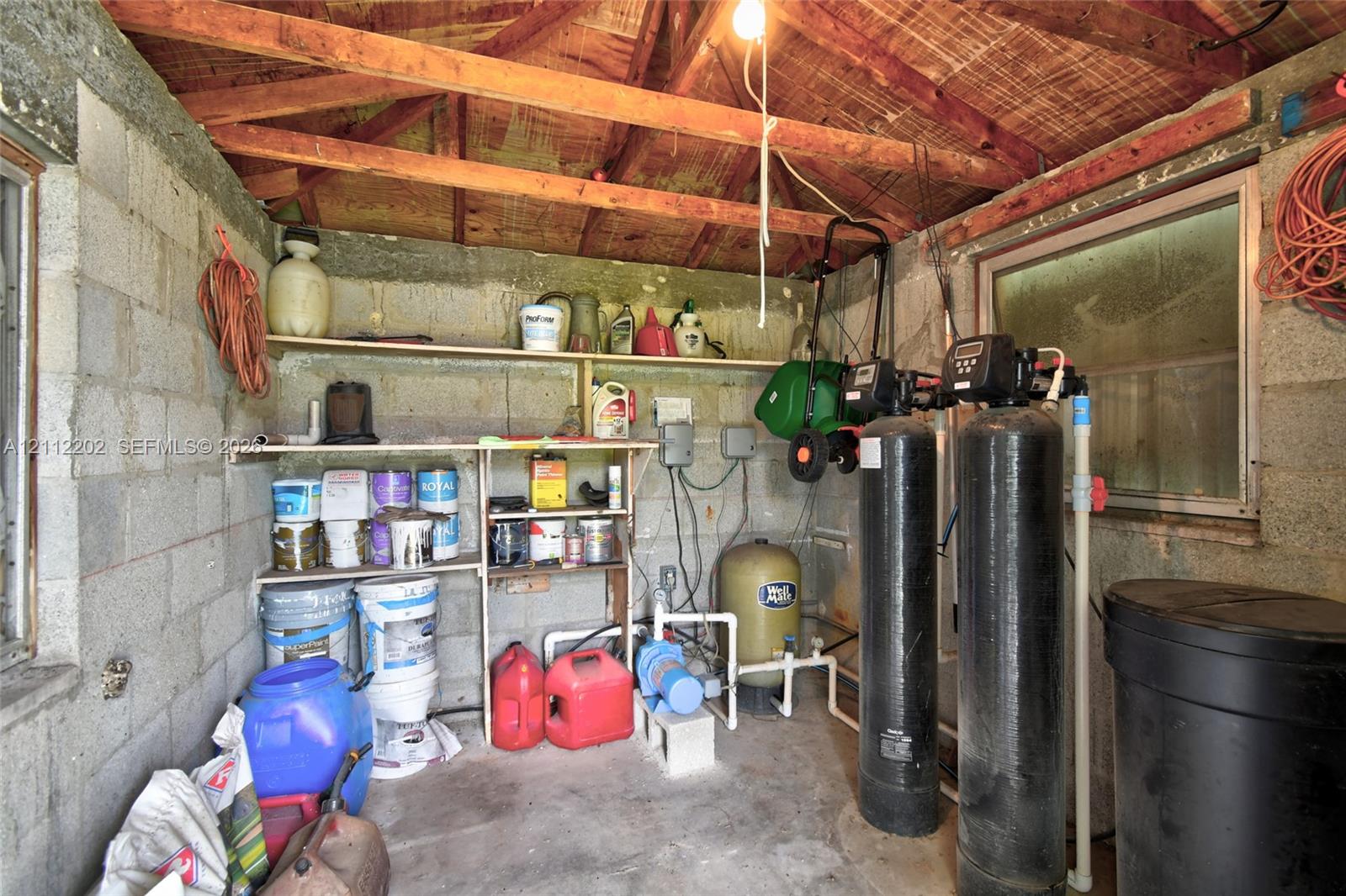 Utility space featuring exposed beam ceiling, concrete block walls, built-in open shelving, and integrated water filtration system