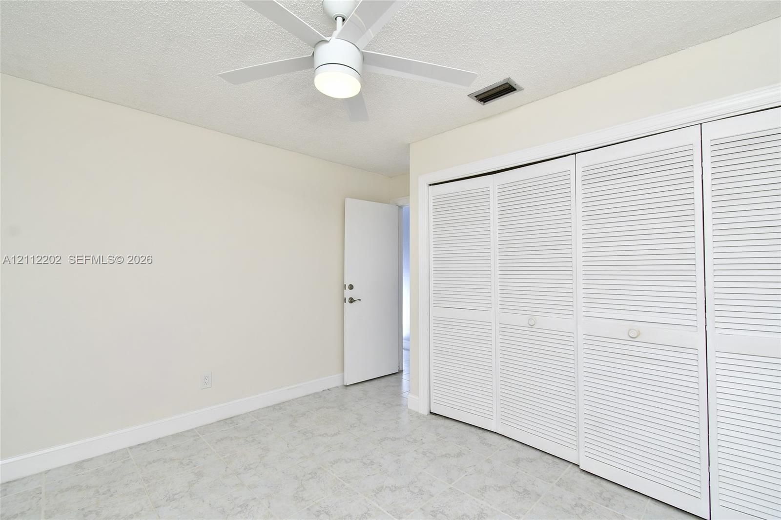 Room featuring neutral-toned walls, tiled flooring, a ceiling fan with integrated lighting, and a triple-panel louvered closet door