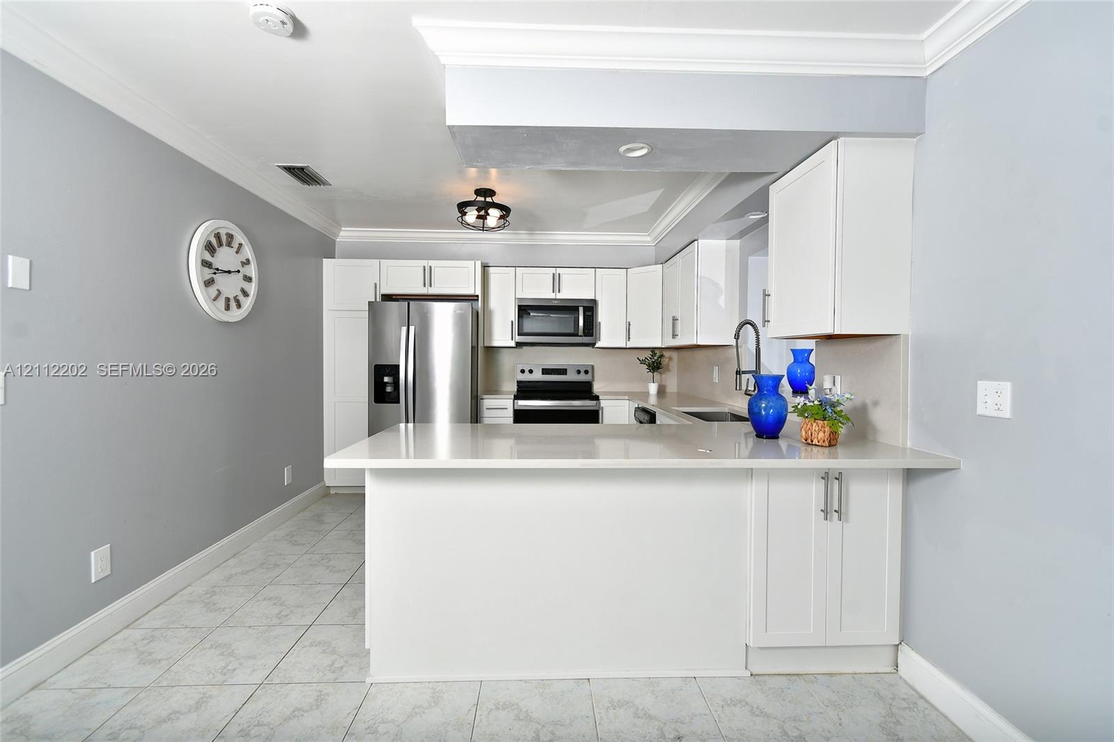 Kitchen featuring white cabinetry, quartz countertops, stainless steel appliances, tile flooring, and crown molding