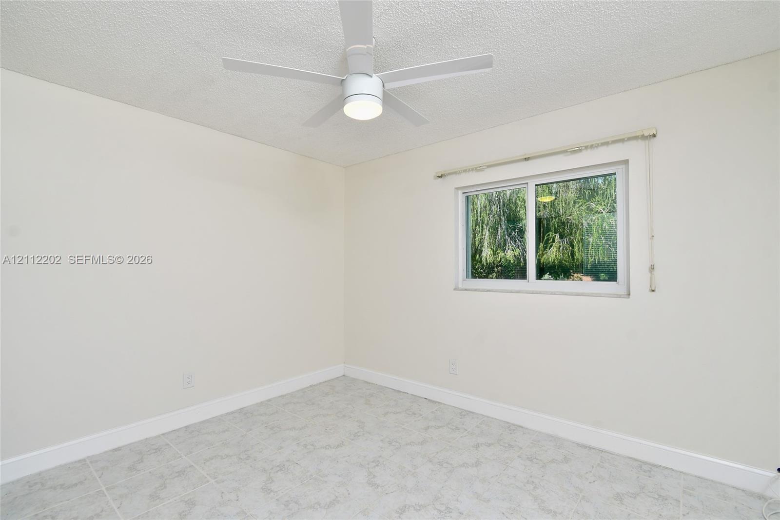 Neutral-toned room featuring a white ceiling fan with integrated lighting, a sliding window with a horizontal blind, and stone-finish tile flooring