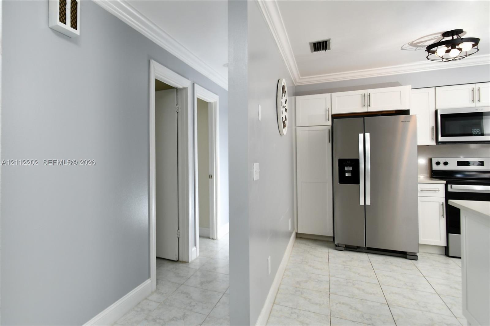 Kitchen featuring white shaker-style cabinetry, stainless steel appliances, tiled flooring, and crown molding