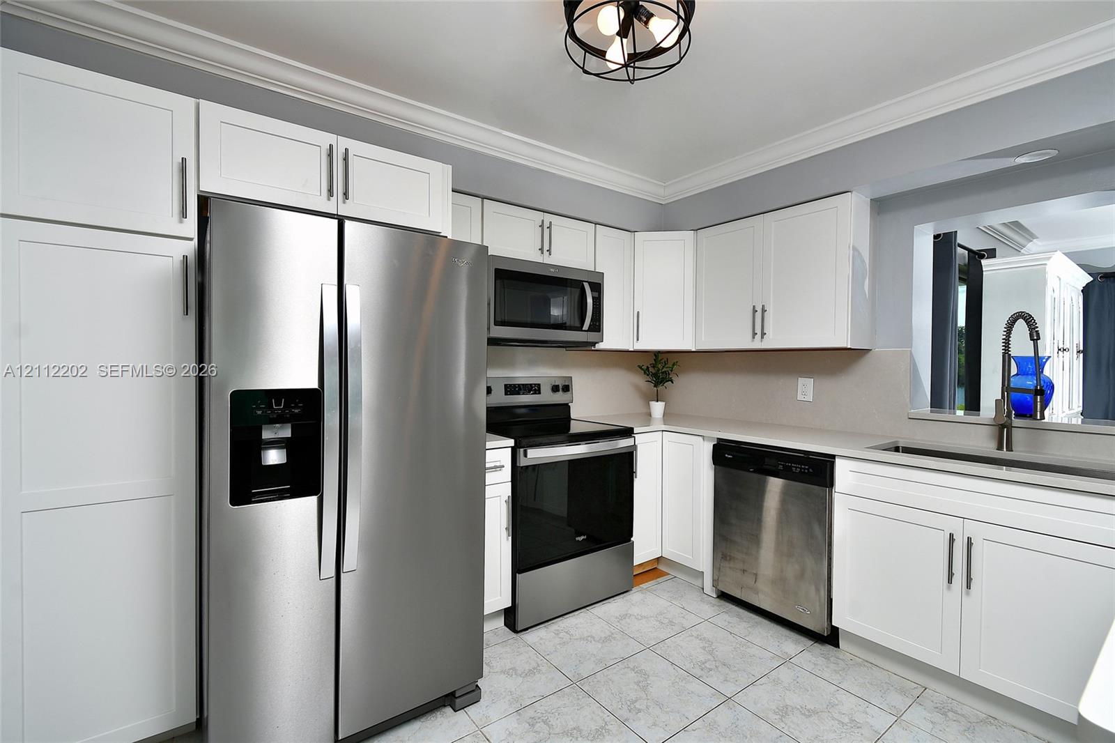 Kitchen featuring white cabinetry, stainless steel appliances, tile flooring, stone-finish countertops, and a ceiling-mounted industrial-style light fixture