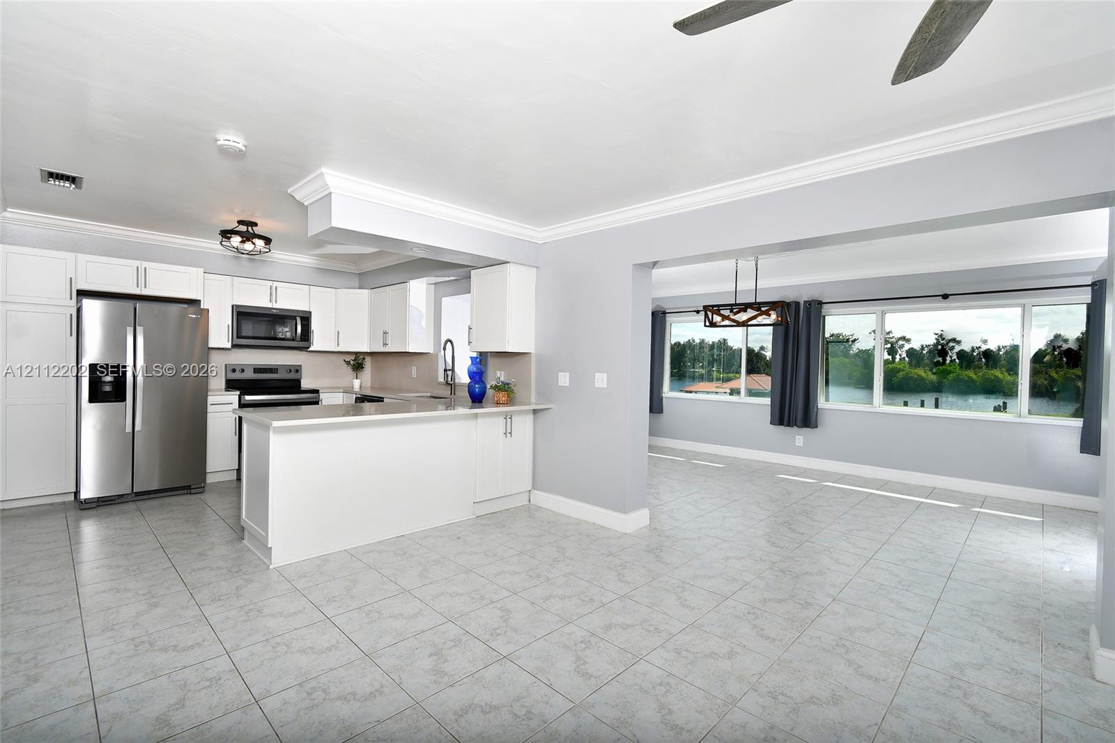 Kitchen featuring white cabinetry, stone countertops, stainless steel appliances, and tile flooring, with large windows providing natural light