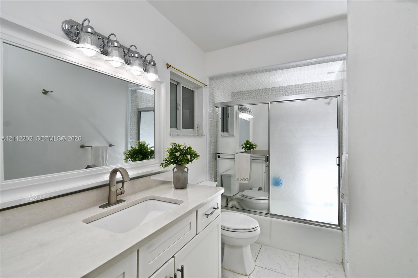 Bathroom featuring a white vanity with a composite countertop, undermount sink, wide-frame mirror, four-light vanity fixture, and a shower-tub combination with sliding glass doors