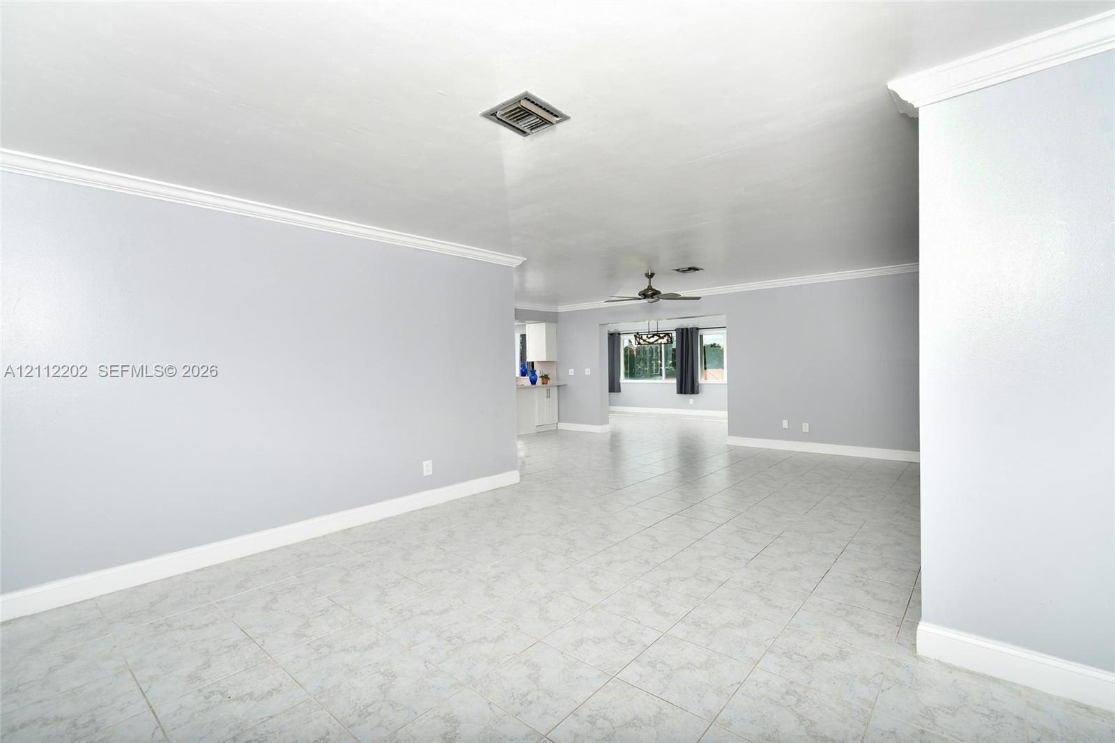 Open-concept interior featuring neutral wall tones, large-format tile flooring, crown molding, and a ceiling fan