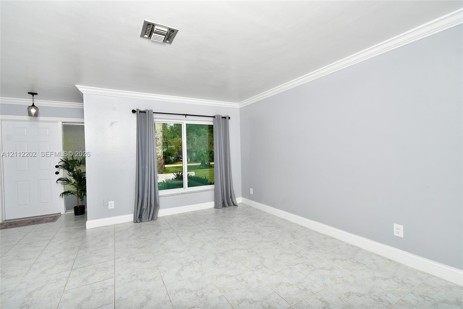 Living area featuring light-toned tile flooring, neutral wall paint, multi-pane window, crown molding, and a paneled entry door