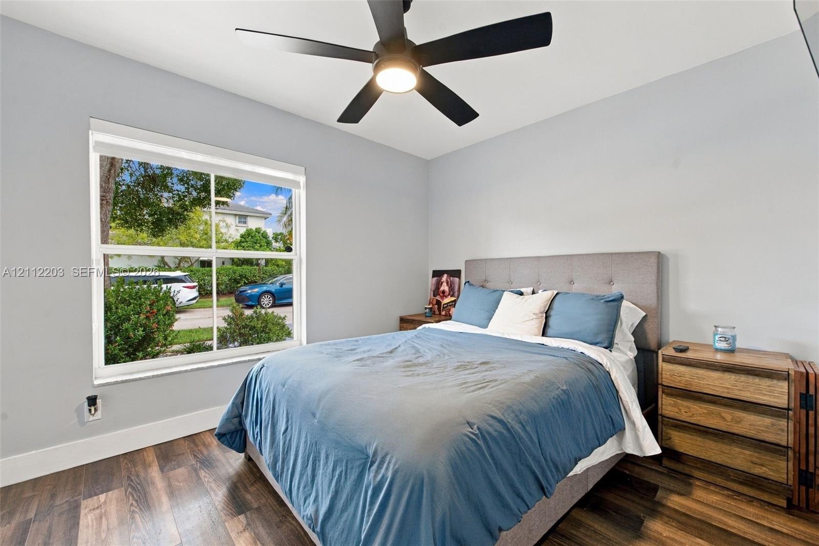 Room featuring wood-finish flooring, a matte black multi-blade ceiling fan with integrated lighting, and a large single-hung window