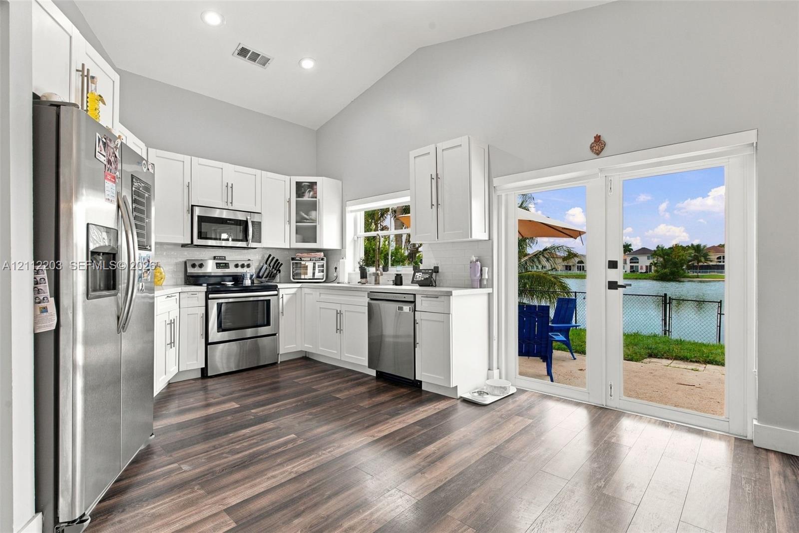 Kitchen featuring white cabinetry, stainless steel appliances, wood-finish flooring, vaulted ceilings, and glass-paneled double doors providing water frontage