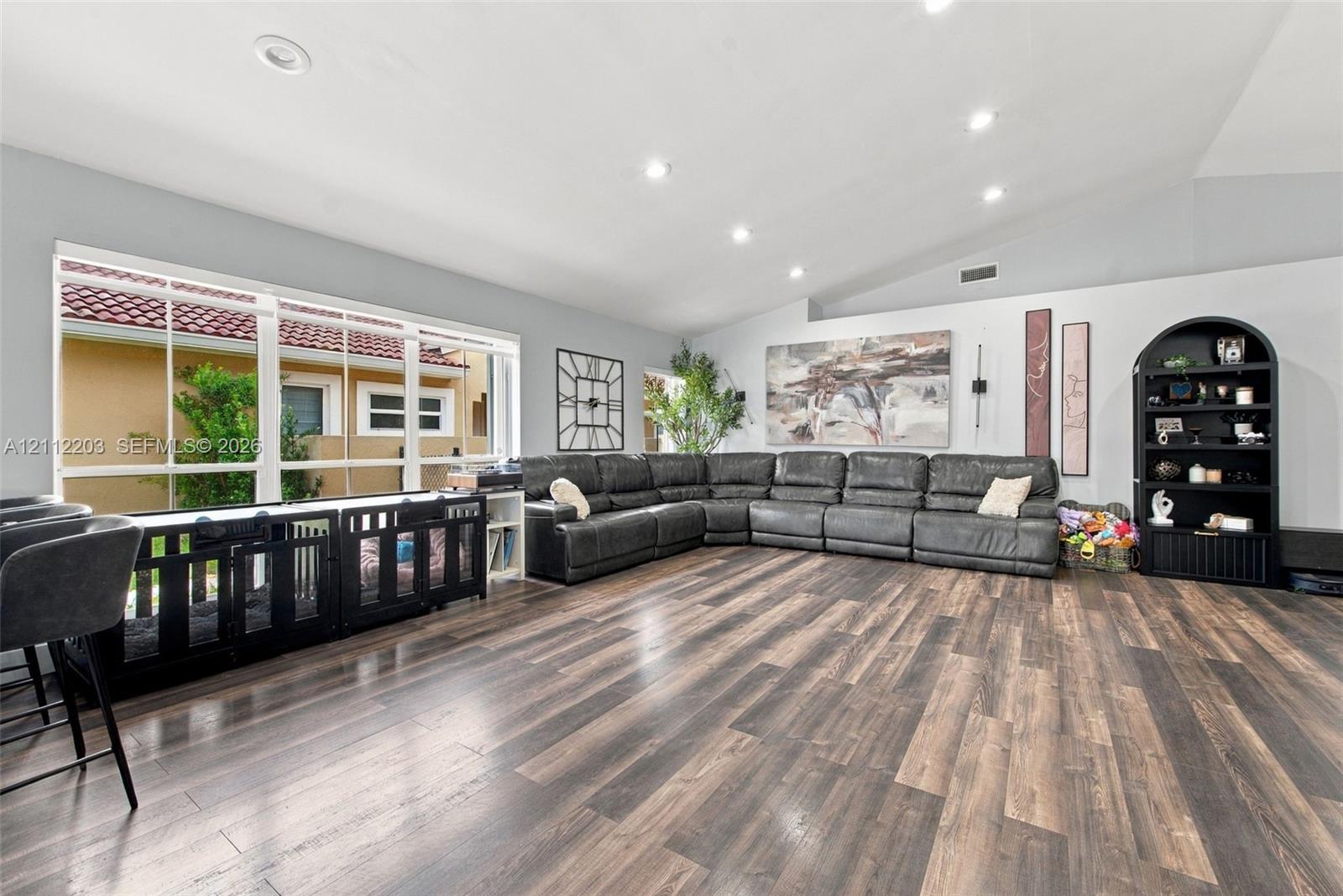 Spacious interior featuring a vaulted ceiling, wood-finish flooring, recessed lighting, and a large multi-pane window