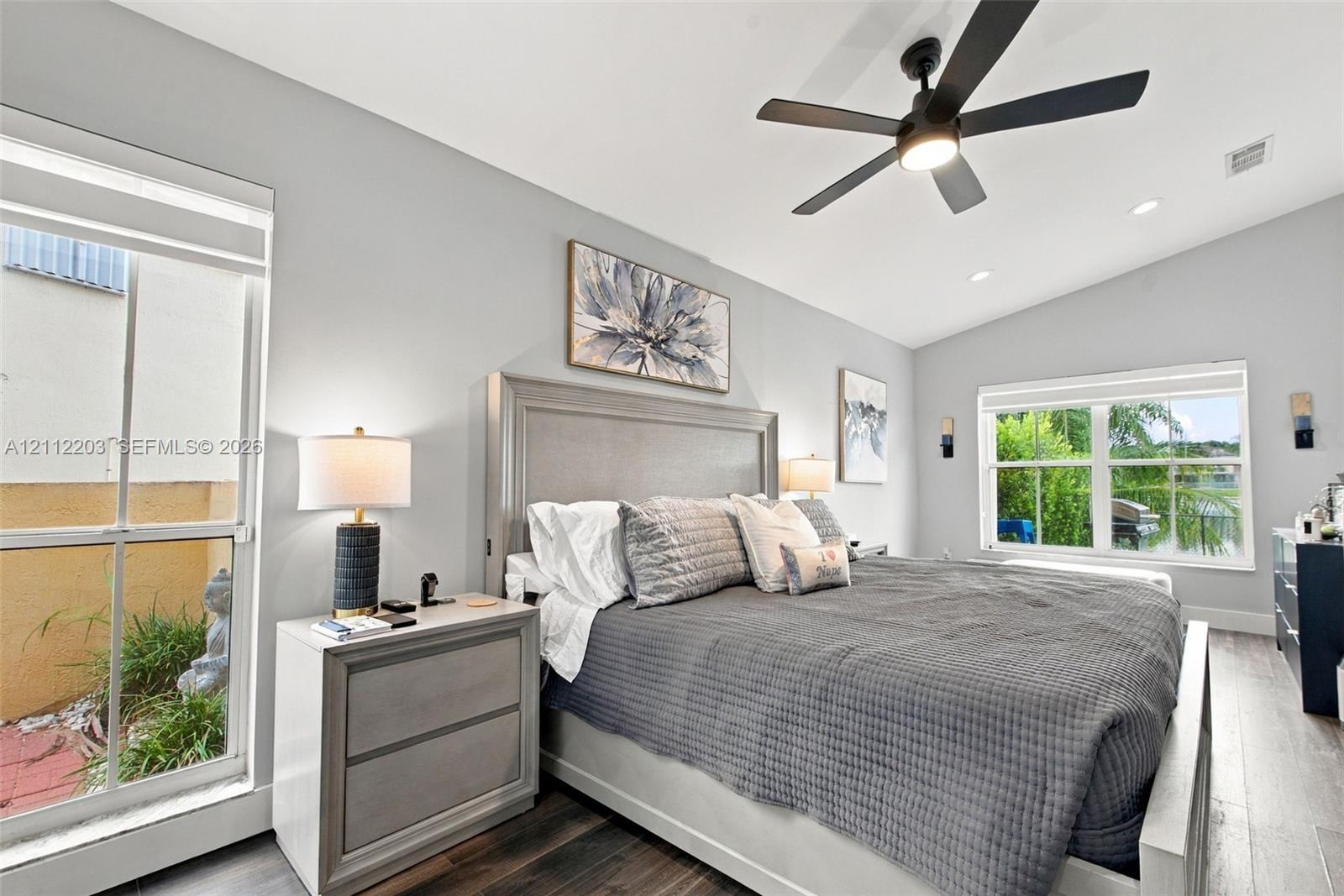 Vaulted ceilings, wood-finish flooring, recessed lighting, matte black ceiling fan, and large windows with multi-pane glazing