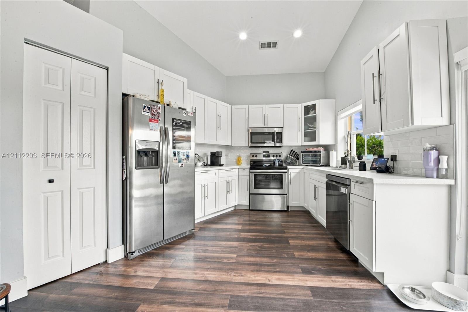 Kitchen featuring white shaker-style cabinetry, stainless steel appliances, white subway tile backsplash, solid-surface countertops, and wood-finish flooring