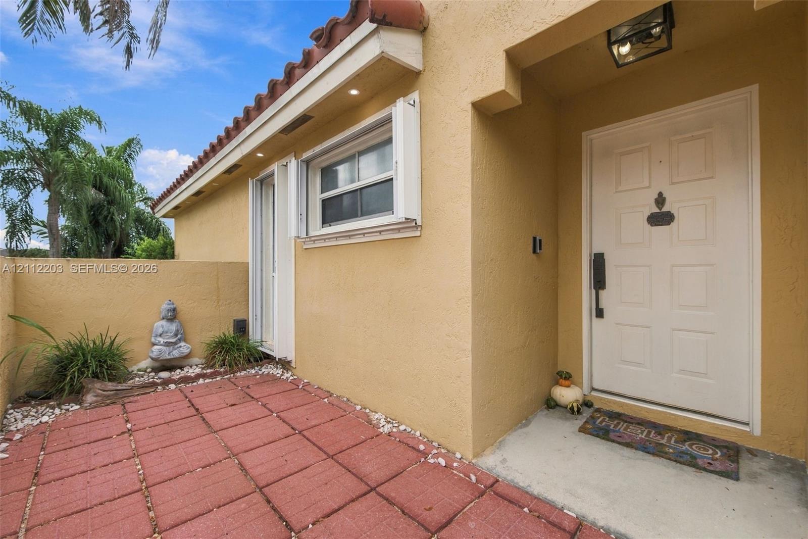 Stucco exterior entryway featuring a terracotta-tiled patio, recessed soffit lighting, and a white paneled front door