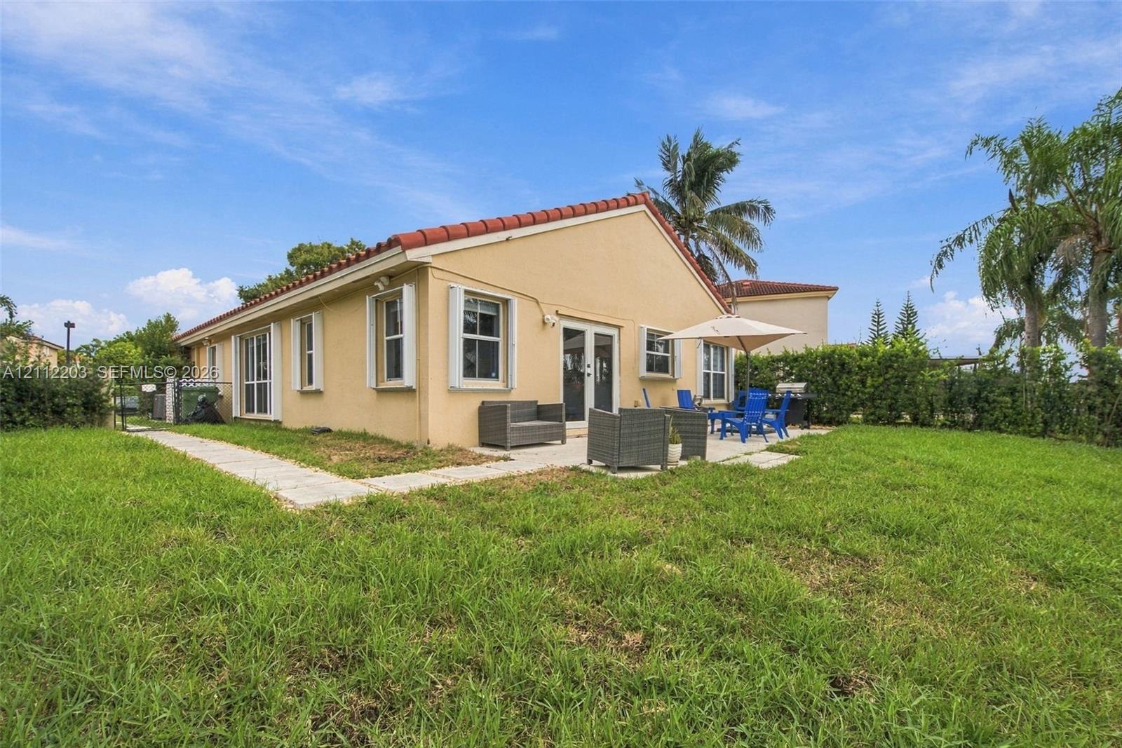 Exterior view of residence featuring a concrete tile roof, light-toned stucco facade, multi-pane windows, and a paved stone patio