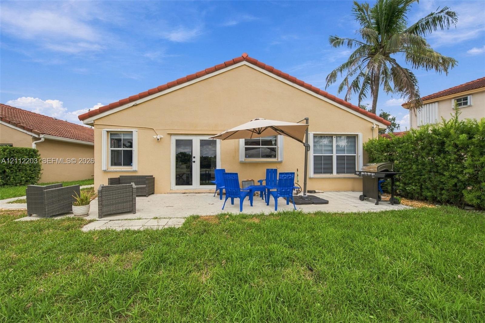 Rear exterior featuring a concrete patio, stucco siding, a tiled roof, and double glass doors