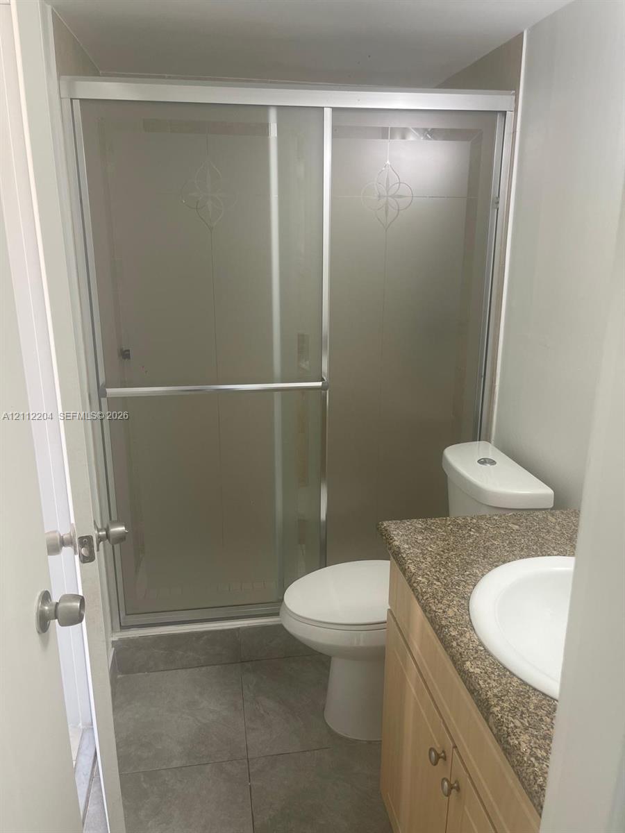 Bathroom featuring a shower stall with a sliding glass door, vanity with a stone-finish countertop, and integrated sink