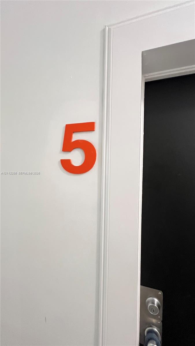 Dimensional numeral identifier featuring a bold orange finish, mounted on a smooth white wall with traditional door casing and metal hardware