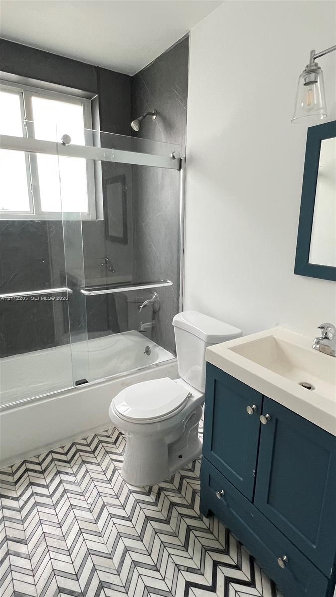 Bathroom featuring herringbone-patterned tile flooring, a blue-finished vanity cabinet with an integrated sink, a glass-enclosed shower, and dark-toned wall tile surround