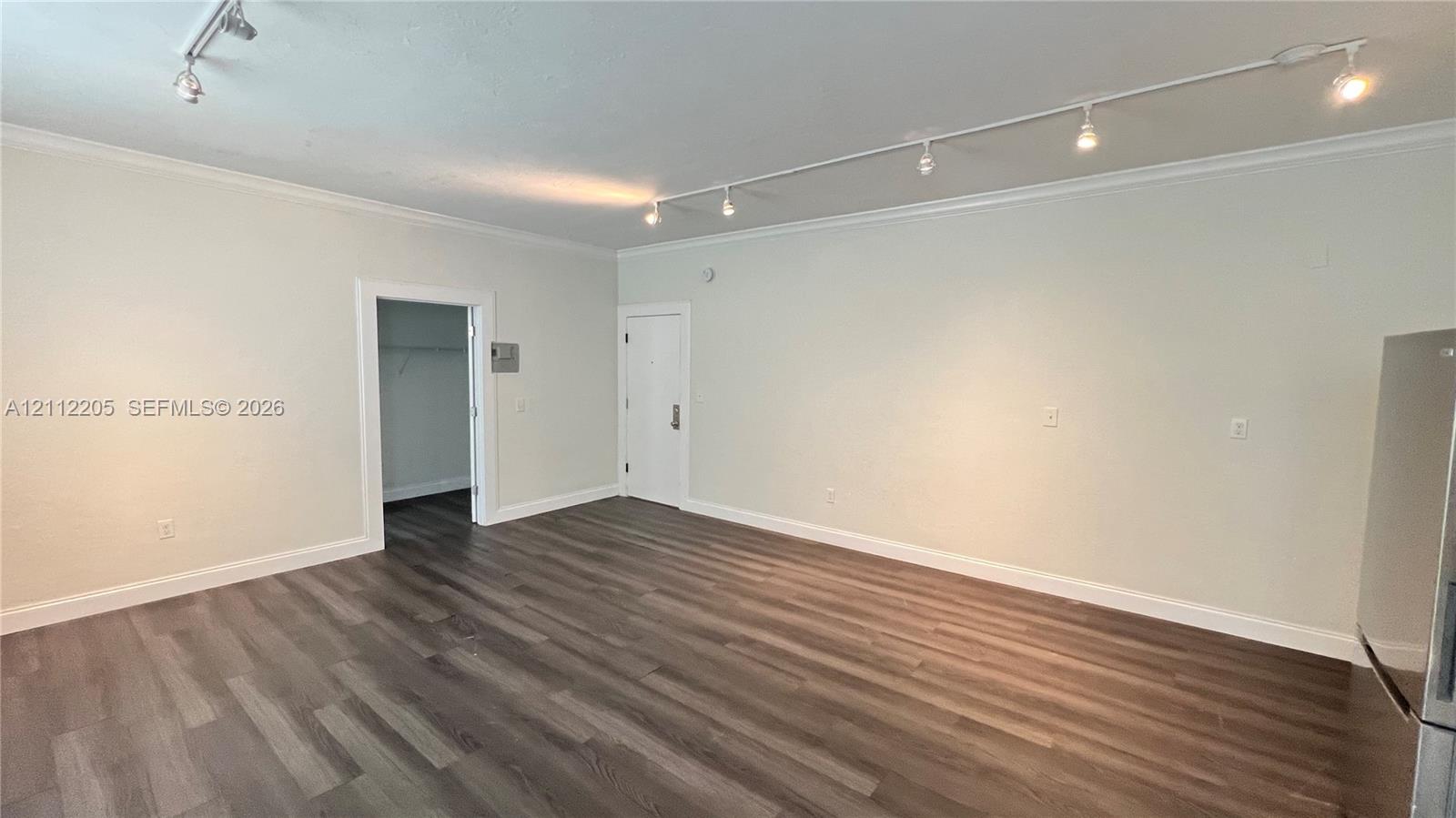 Wood-finish flooring, adjustable track lighting, neutral wall palette, and crown molding