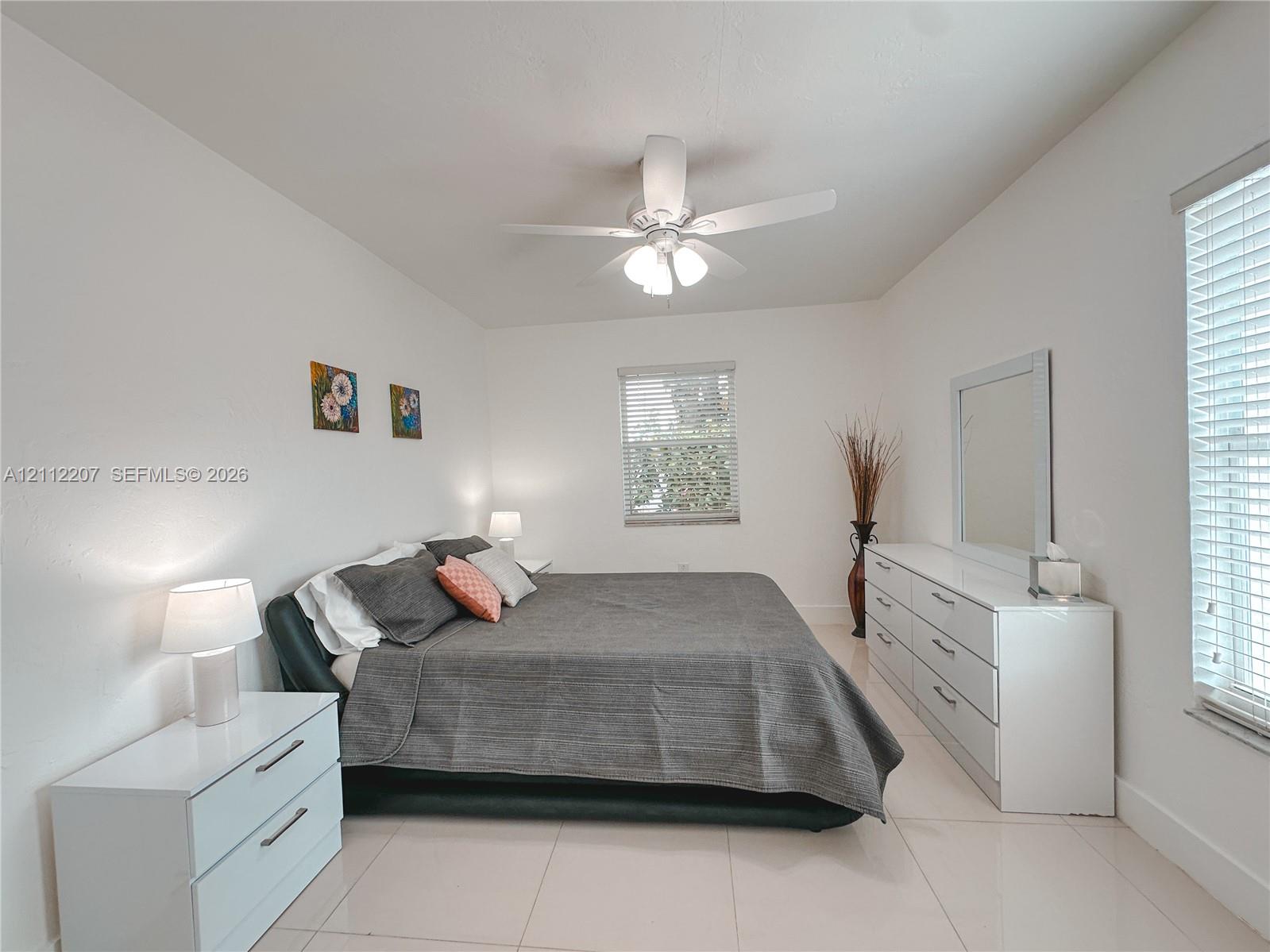 Spacious room featuring neutral tile flooring, a multi-blade ceiling fan with integrated lighting, and multiple windows fitted with horizontal blinds