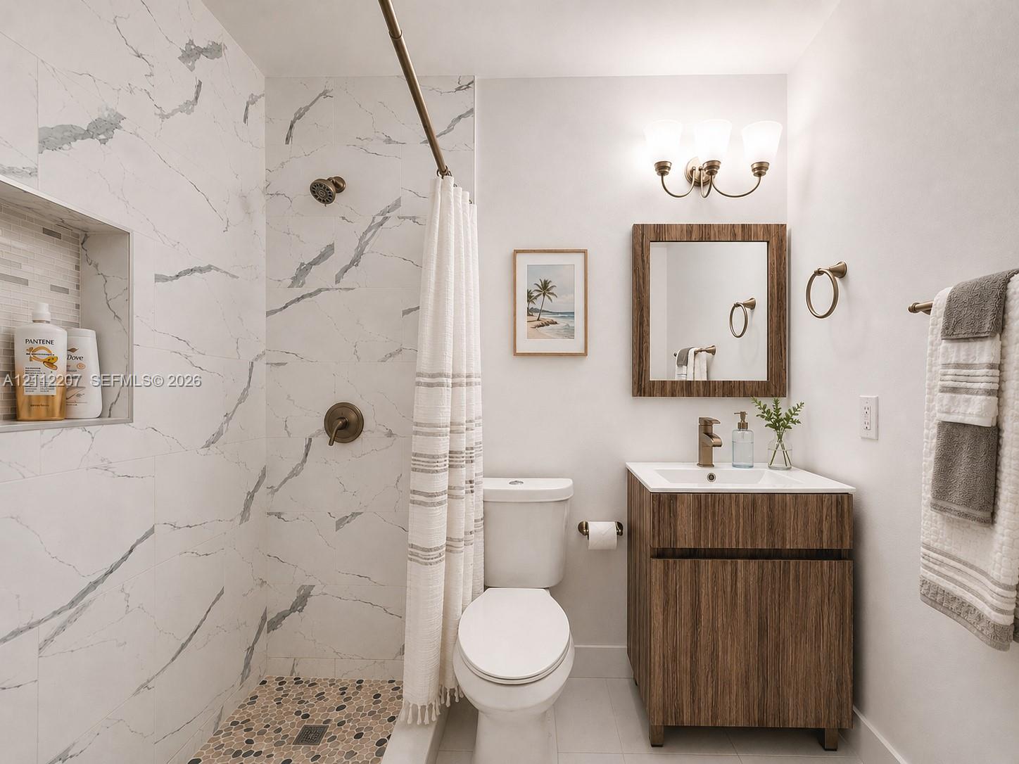 Bathroom featuring a walk-in shower with stone-patterned wall tile, a recessed storage niche, a pebble-finish floor, a wood-finish vanity with a rectangular sink, and a three-light wall-mounted fixture