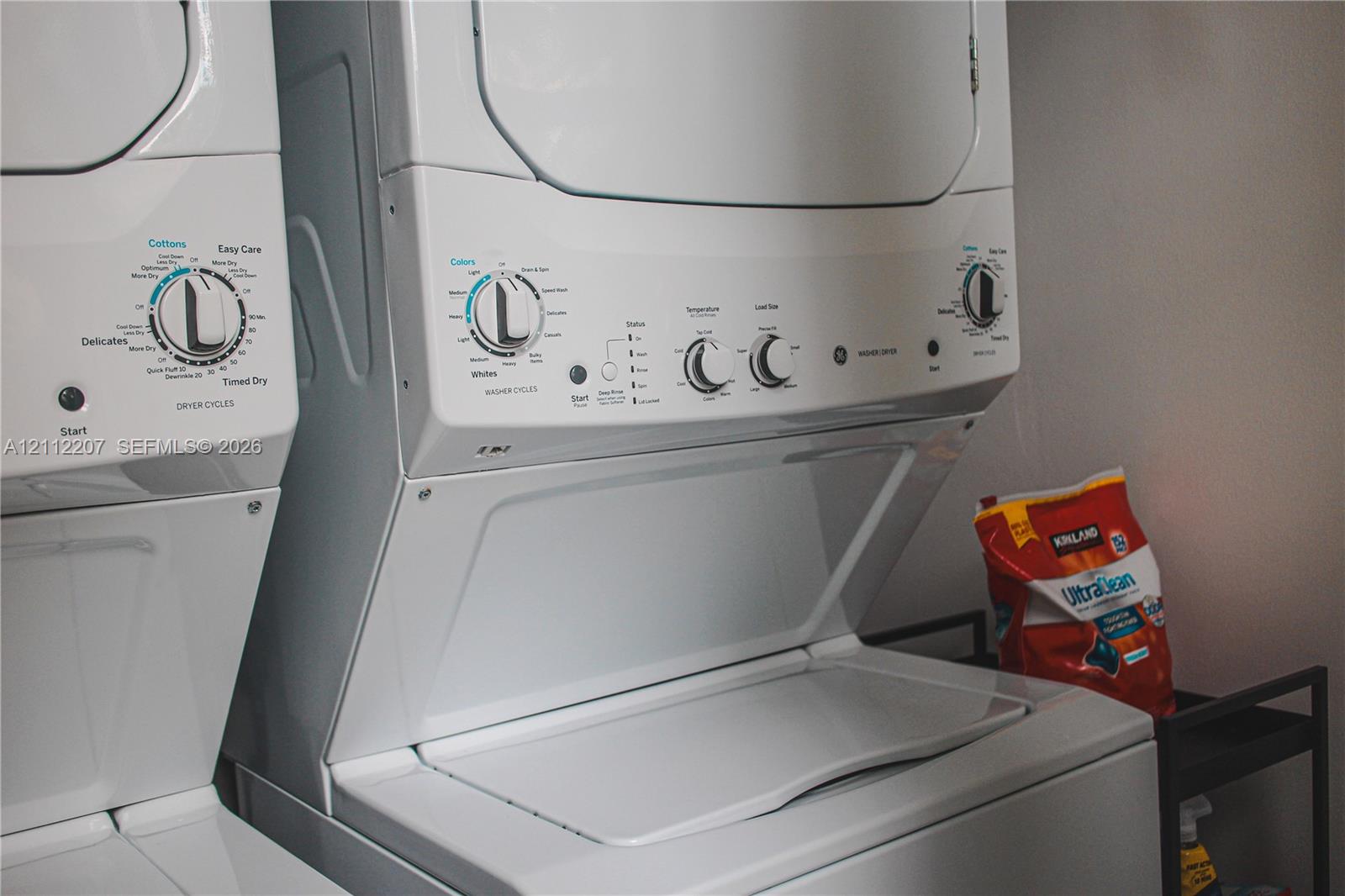 Stacked white laundry appliance unit featuring a top-load washer and front-control drying interface