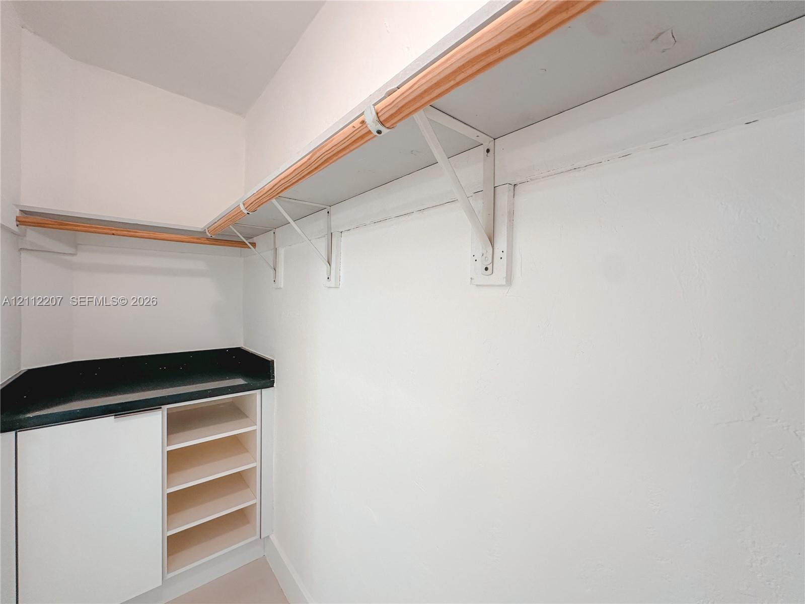 Built-in cabinetry with integrated open shelving, solid surface countertop, and wall-mounted wood-finish clothing rods with metal supports
