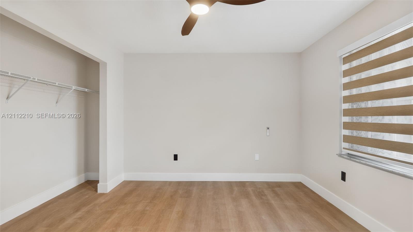 Room featuring wood-finish flooring, a ceiling fan with integrated lighting, a built-in wire closet shelving system, and window treatments