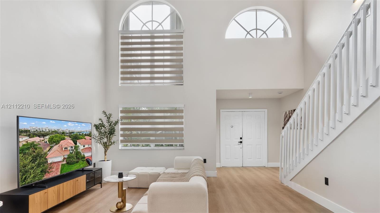 Double-height ceilings, arched upper windows, wood-finish flooring, staircase with white vertical balusters, and double-door entry