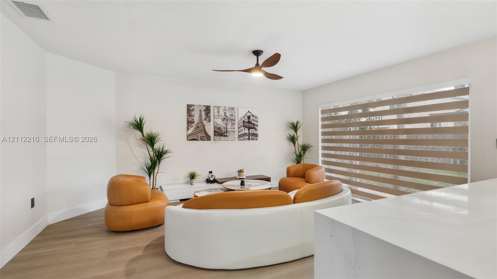 Living area featuring wood-finish flooring, a modern three-blade ceiling fan, and large windows with horizontal banded shades