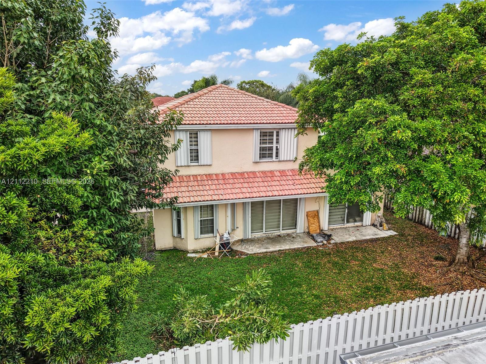 Two-story residence featuring a terracotta-tiled roof, light-colored stucco exterior, sliding glass doors, and a private rear yard enclosed by a white picket fence