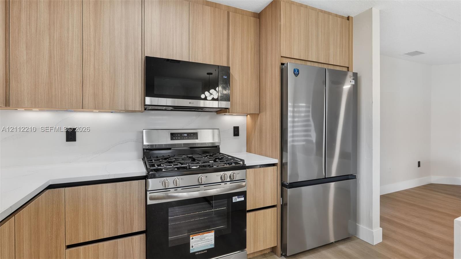 Kitchen featuring flat-panel wood-finish cabinetry, white solid-surface countertops, stainless steel appliances, and integrated under-cabinet lighting