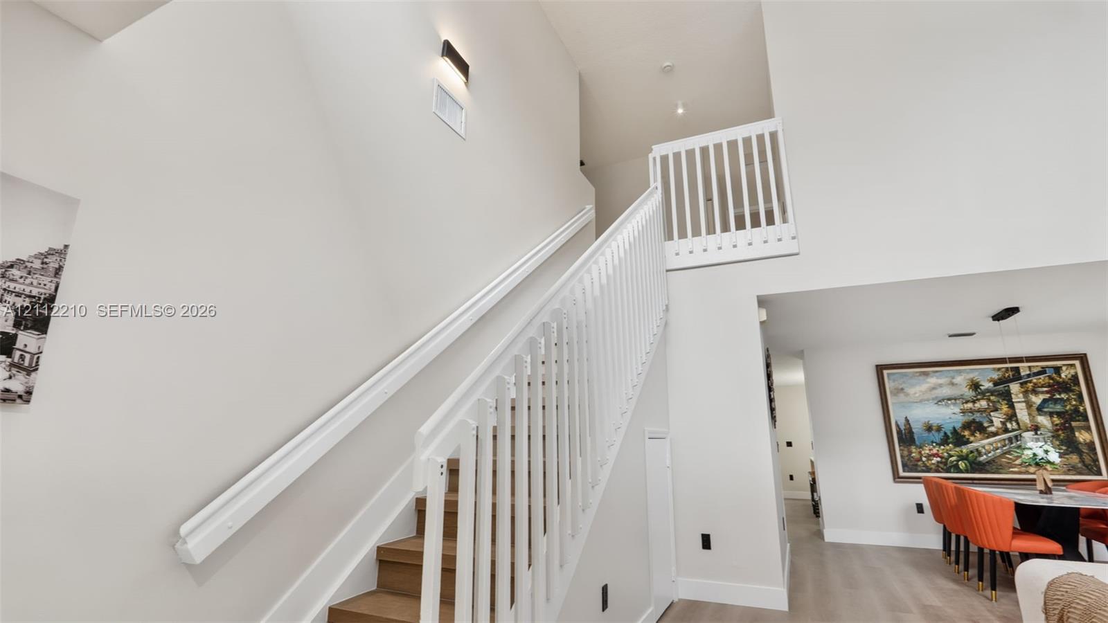 Staircase featuring wood-finish treads, a white handrail, and white vertical balusters under a high ceiling