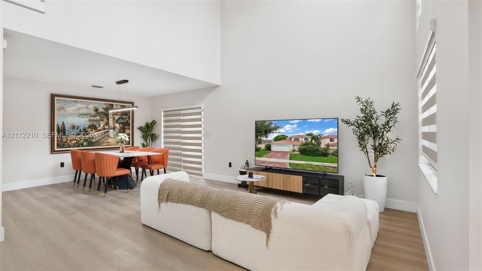 High-ceiling living area featuring wood-finish flooring, neutral wall paint, and horizontal zebra blinds
