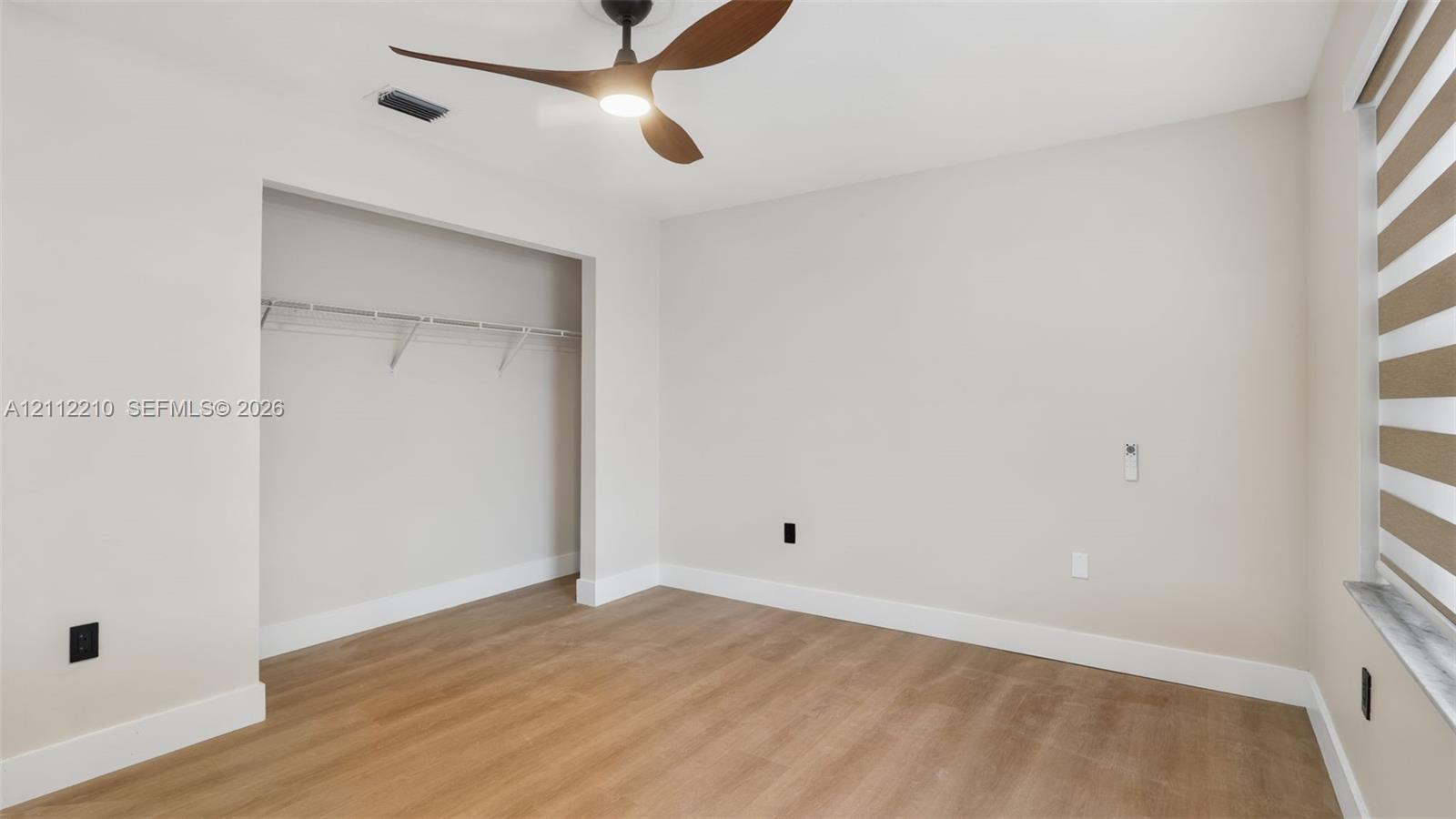 Interior space featuring wood-finish flooring, a contemporary three-blade ceiling fan with integrated lighting, and a built-in reach-in closet with wire shelving