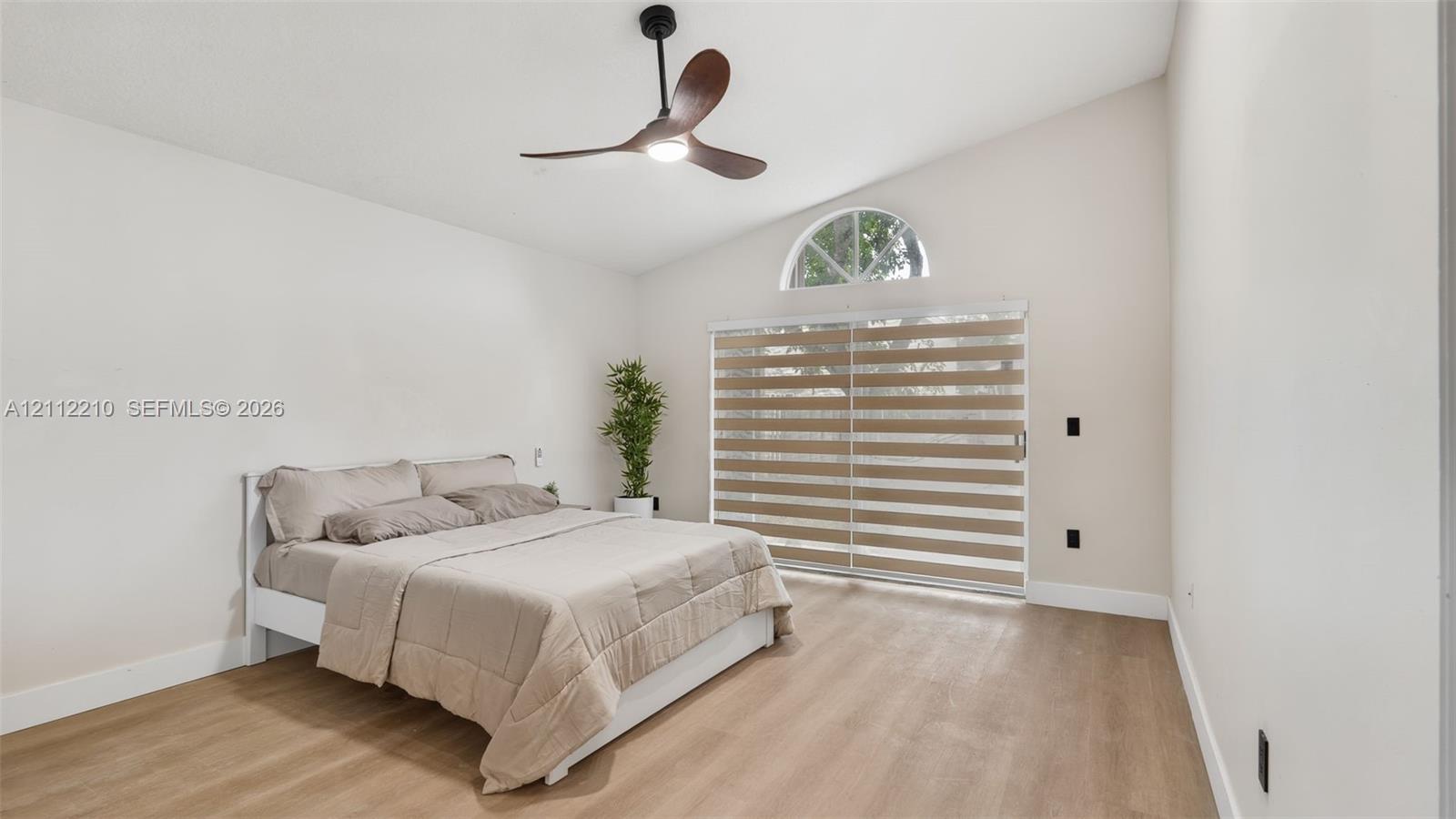 Vaulted ceiling featuring a three-blade ceiling fan, wood-finish flooring, and a sliding glass door topped with a semicircular window