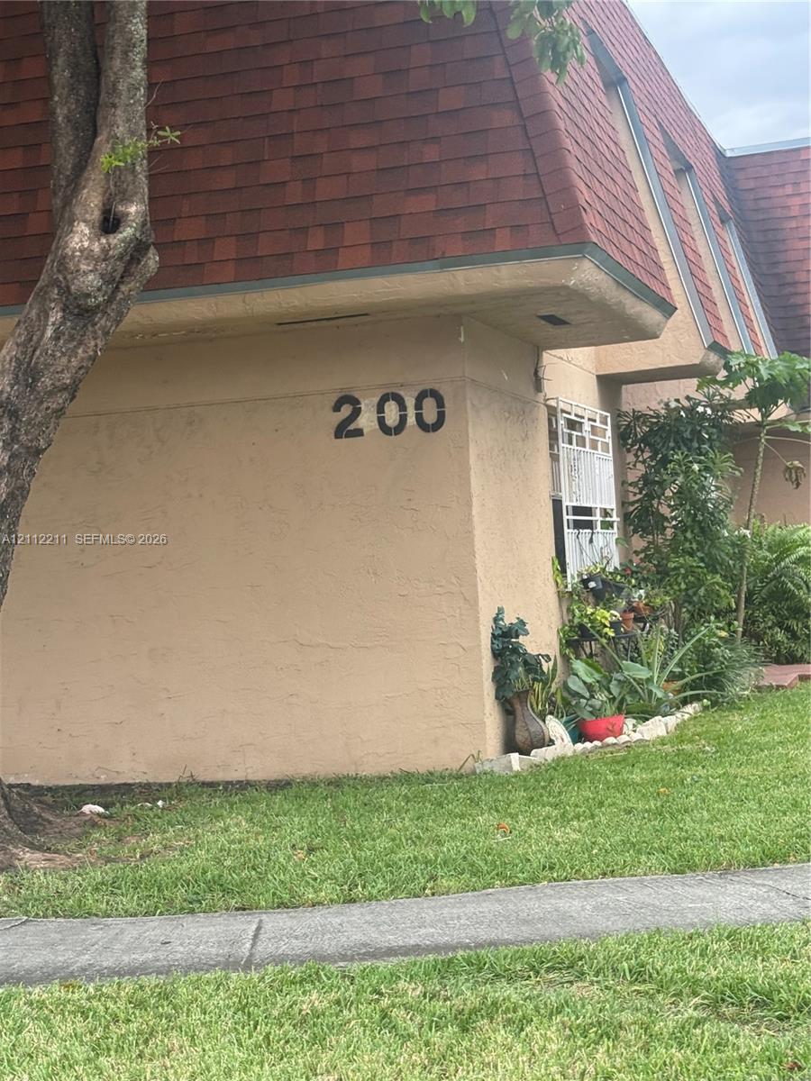Exterior facade featuring textured stucco finish, dark red asphalt shingle mansard roof, and metal window security grate